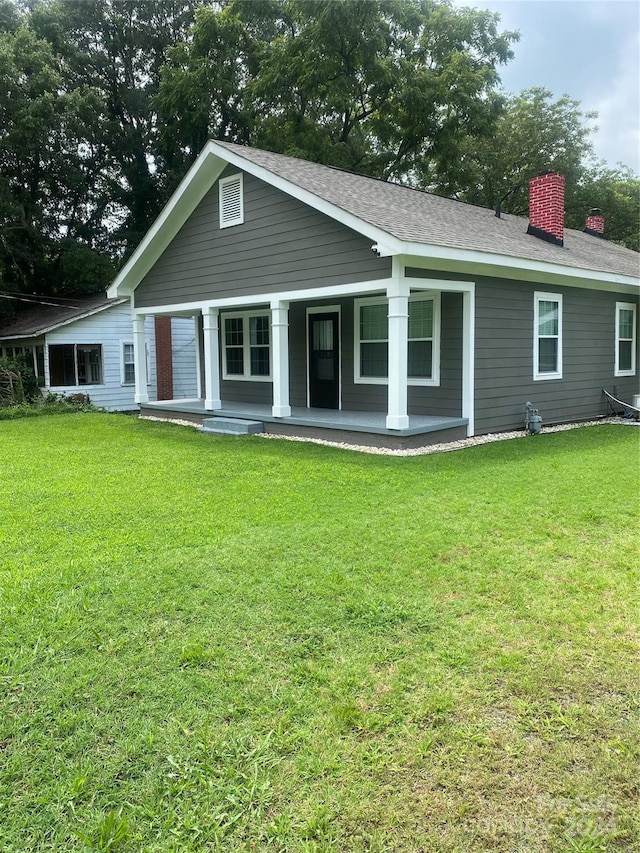 back of house featuring a yard, covered porch, roof with shingles, and a chimney