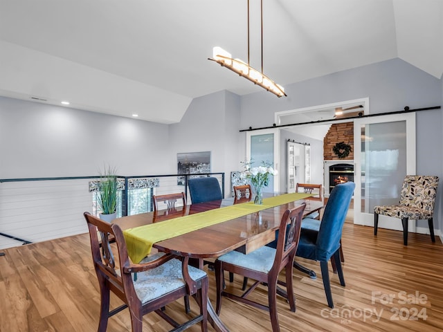 dining room with hardwood / wood-style flooring, a barn door, and vaulted ceiling