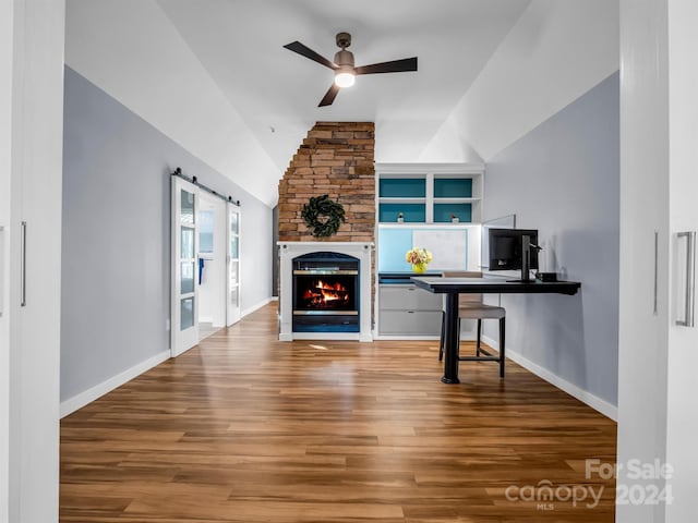 interior space with ceiling fan, lofted ceiling, a barn door, hardwood / wood-style flooring, and built in shelves