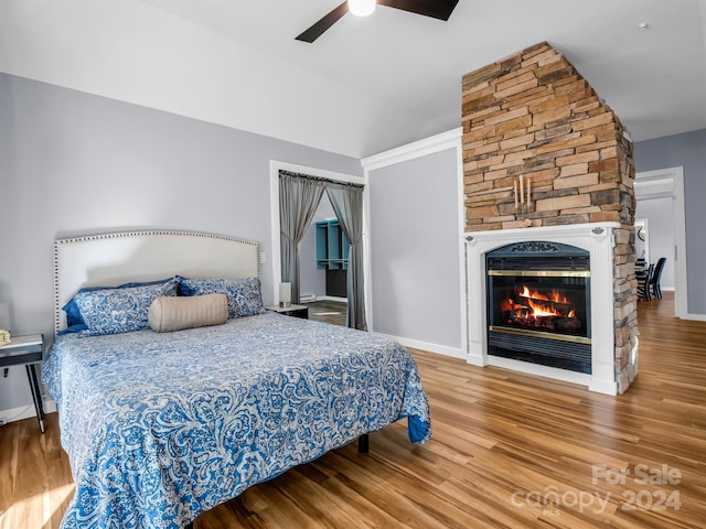 bedroom featuring vaulted ceiling, ceiling fan, wood-type flooring, and a stone fireplace