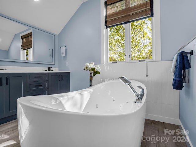 bathroom featuring vaulted ceiling, a tub to relax in, hardwood / wood-style floors, and vanity