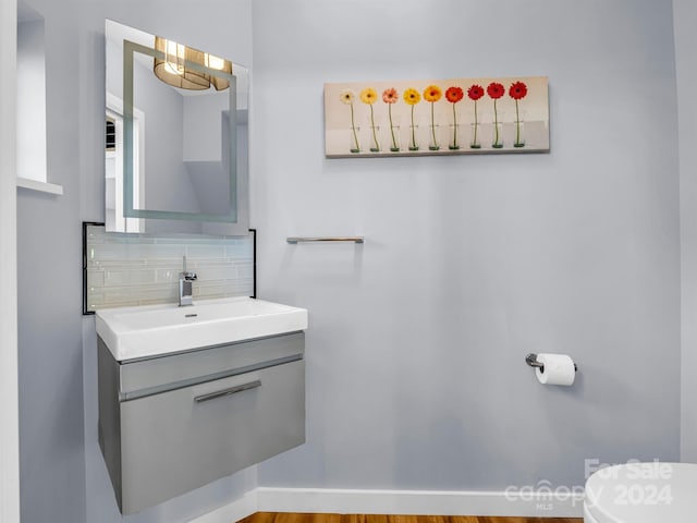 bathroom featuring hardwood / wood-style flooring, toilet, vanity, and tasteful backsplash