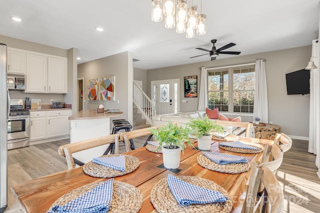 dining space with ceiling fan with notable chandelier and light hardwood / wood-style flooring