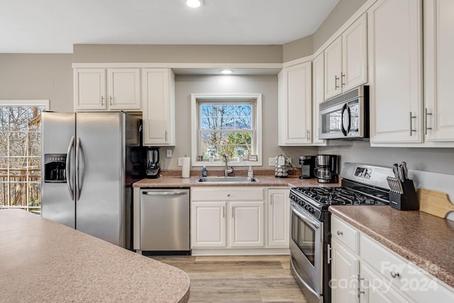 kitchen with white cabinets, appliances with stainless steel finishes, light hardwood / wood-style flooring, and sink