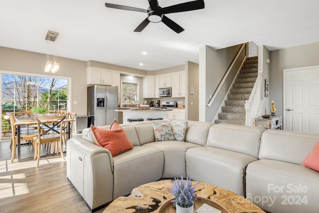 living room featuring ceiling fan with notable chandelier and light wood-type flooring