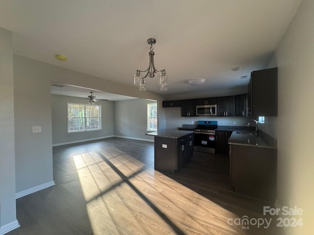 kitchen featuring dark hardwood / wood-style flooring, ceiling fan with notable chandelier, stainless steel appliances, pendant lighting, and a kitchen island