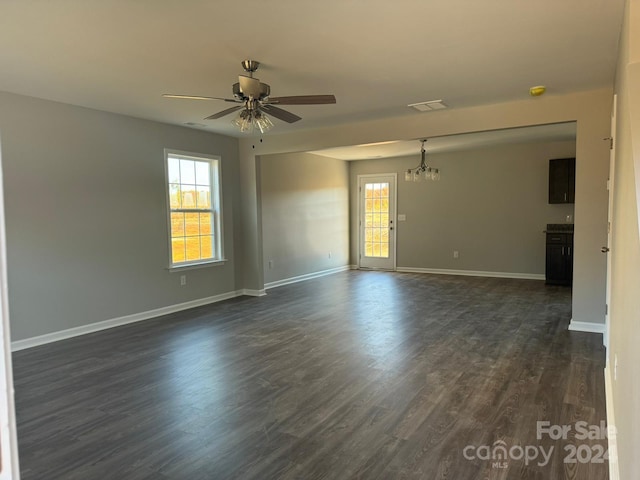 empty room featuring ceiling fan with notable chandelier, a wealth of natural light, and dark hardwood / wood-style floors