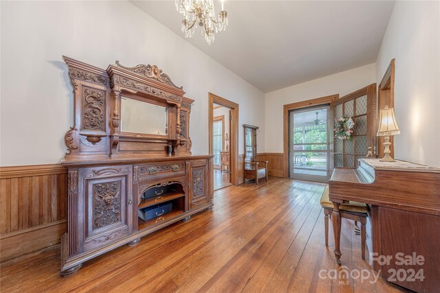 foyer with an inviting chandelier, wood walls, wood-type flooring, and vaulted ceiling