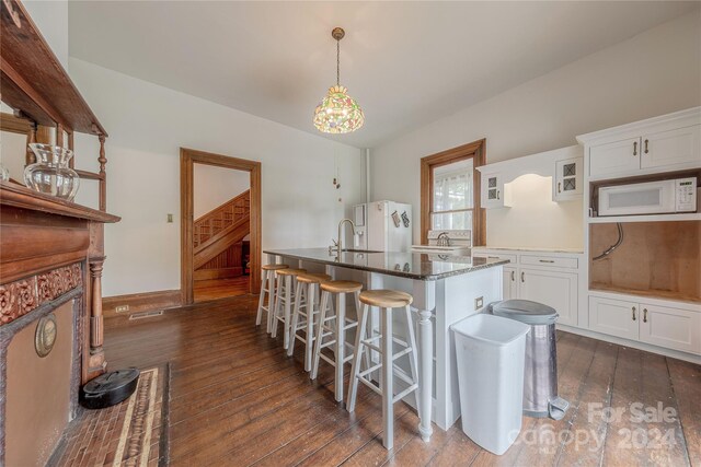 kitchen featuring hanging light fixtures, white cabinetry, a kitchen bar, dark stone counters, and dark wood-type flooring