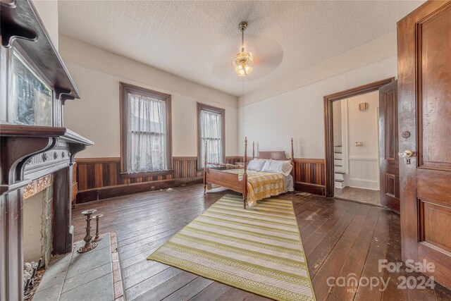 bedroom featuring ceiling fan, a textured ceiling, wooden walls, and dark hardwood / wood-style floors