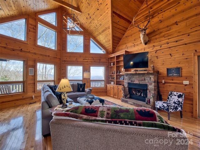 living room featuring wood walls, high vaulted ceiling, a stone fireplace, wood ceiling, and light wood-type flooring