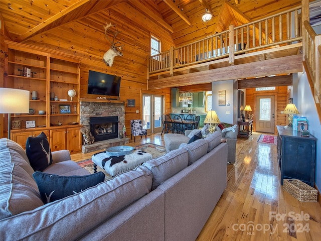 living room with beamed ceiling, a stone fireplace, wooden walls, wooden ceiling, and light hardwood / wood-style flooring