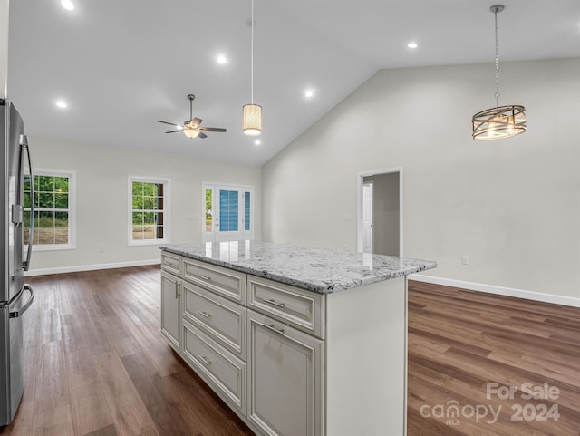 kitchen featuring a center island, dark wood-type flooring, hanging light fixtures, light stone countertops, and stainless steel refrigerator