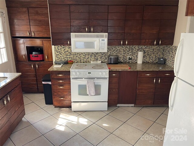 kitchen featuring dark brown cabinetry, white appliances, tasteful backsplash, and dark stone counters