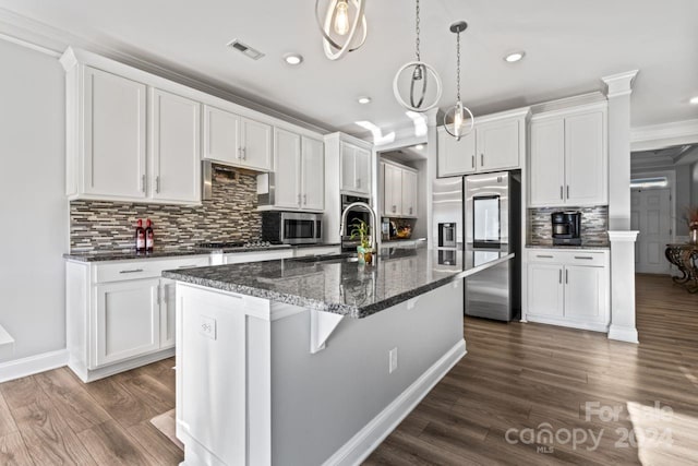 kitchen with backsplash, decorative light fixtures, dark hardwood / wood-style flooring, crown molding, and a kitchen island with sink