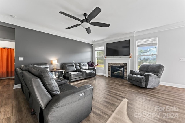 living room with a healthy amount of sunlight, crown molding, dark wood-type flooring, a stone fireplace, and ceiling fan