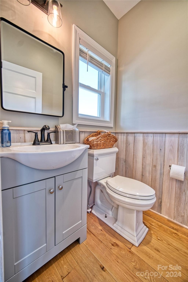 bathroom featuring wood-type flooring, wood walls, vanity, and toilet