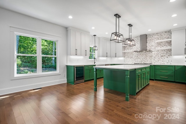 kitchen featuring a kitchen island, green cabinets, white cabinets, wall chimney exhaust hood, and beverage cooler