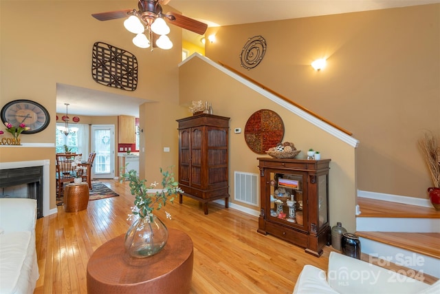 living room with ceiling fan, a high ceiling, and light wood-type flooring