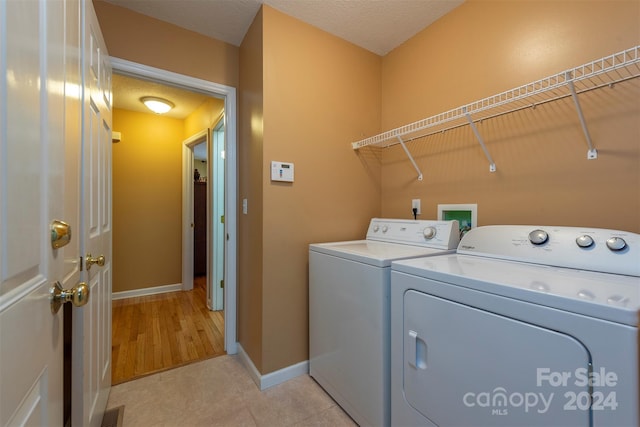 clothes washing area featuring a textured ceiling, light tile floors, hookup for a washing machine, and washing machine and clothes dryer