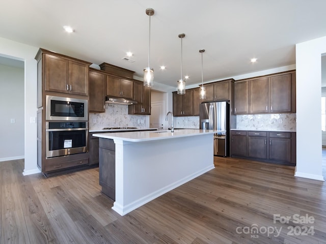 kitchen featuring dark brown cabinetry, stainless steel appliances, a kitchen island with sink, decorative light fixtures, and hardwood / wood-style floors