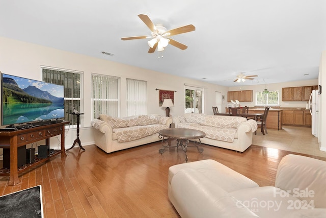 living room with light hardwood / wood-style floors, ceiling fan, and a healthy amount of sunlight