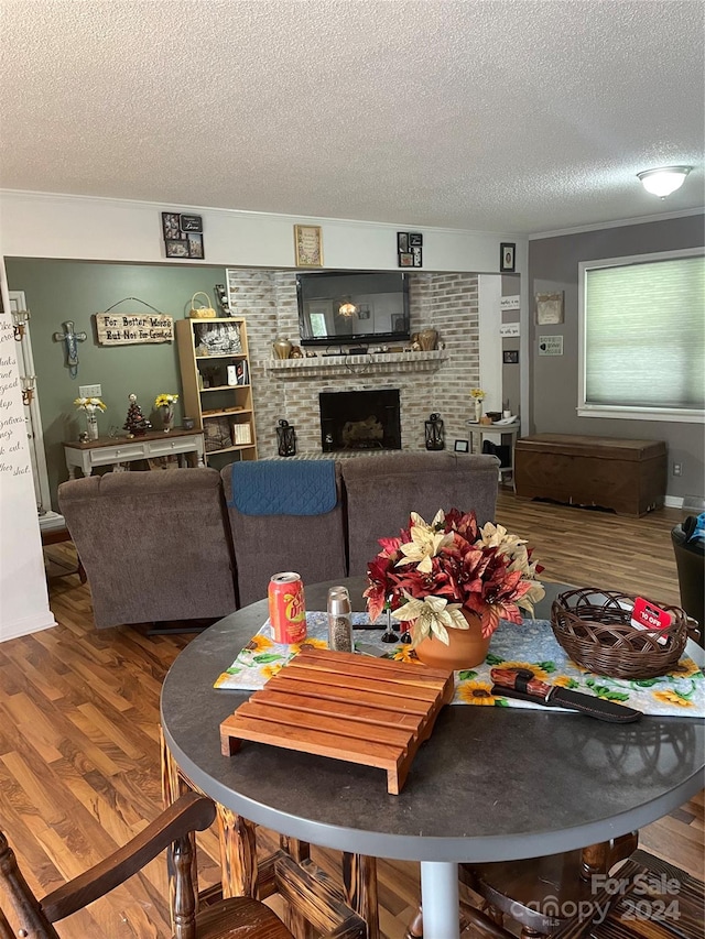 dining area featuring hardwood / wood-style flooring, brick wall, a brick fireplace, and a textured ceiling