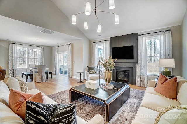 living room with light hardwood / wood-style flooring, a fireplace, a notable chandelier, and lofted ceiling