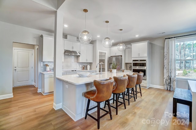 kitchen featuring a kitchen island with sink, light hardwood / wood-style floors, white cabinetry, stainless steel appliances, and pendant lighting