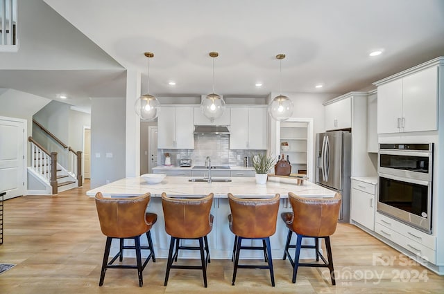 kitchen with tasteful backsplash, light hardwood / wood-style floors, stainless steel appliances, and an island with sink