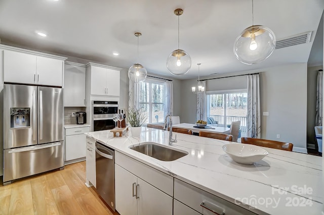 kitchen featuring hanging light fixtures, white cabinetry, stainless steel appliances, sink, and light hardwood / wood-style floors