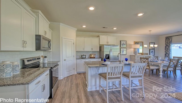 kitchen with light stone countertops, light hardwood / wood-style flooring, stainless steel appliances, a kitchen island with sink, and pendant lighting