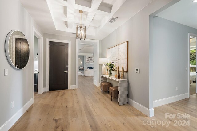 entrance foyer featuring light wood-type flooring, coffered ceiling, an inviting chandelier, and beamed ceiling