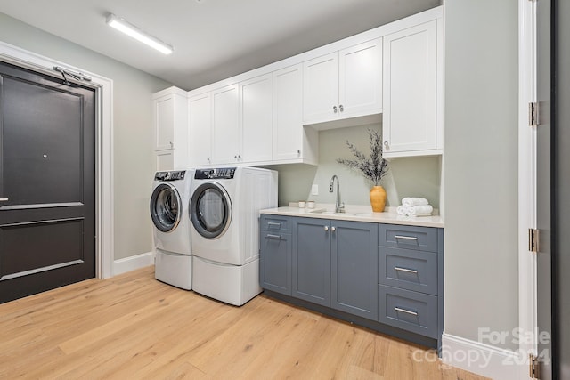 laundry room with cabinets, washing machine and clothes dryer, sink, and light hardwood / wood-style floors