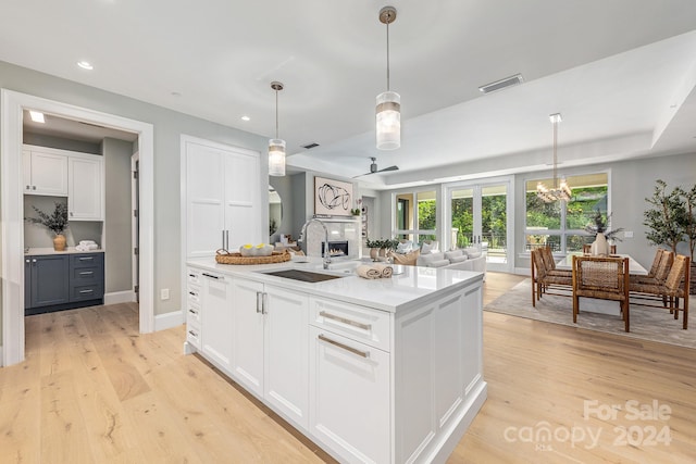 kitchen featuring a center island with sink, light hardwood / wood-style flooring, pendant lighting, sink, and white cabinets