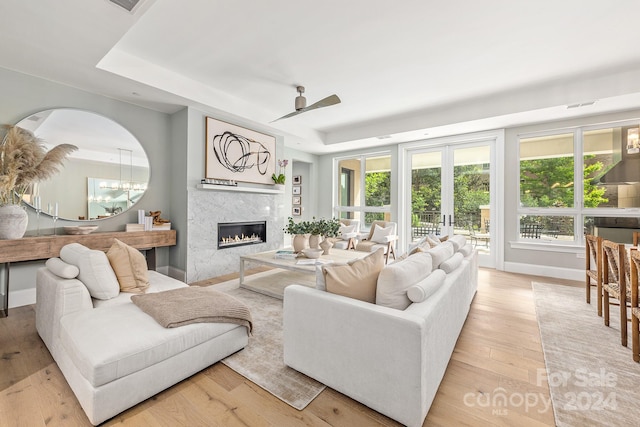 living room with a tray ceiling, ceiling fan, a tile fireplace, and light hardwood / wood-style flooring