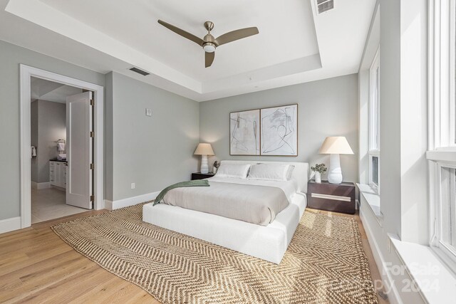 bedroom with ceiling fan, a tray ceiling, and light hardwood / wood-style floors