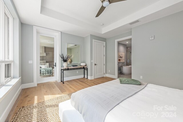 bedroom featuring light wood-type flooring, a tray ceiling, ceiling fan, and ensuite bathroom