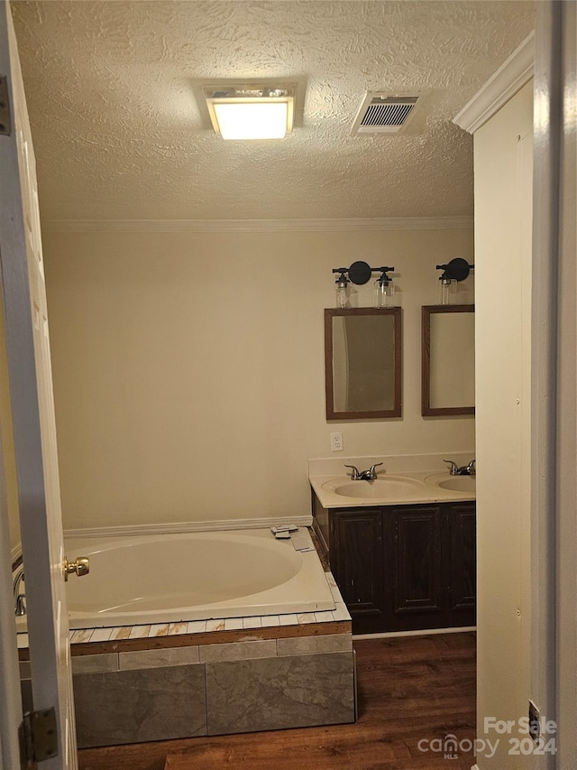 bathroom with wood-type flooring, a relaxing tiled bath, dual vanity, and a textured ceiling