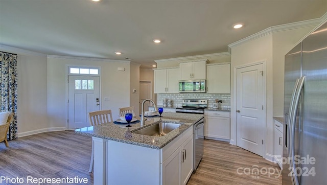 kitchen featuring appliances with stainless steel finishes, white cabinetry, a center island with sink, and light wood-type flooring