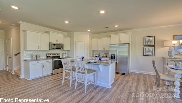 kitchen with white cabinets, backsplash, appliances with stainless steel finishes, light stone counters, and light hardwood / wood-style floors