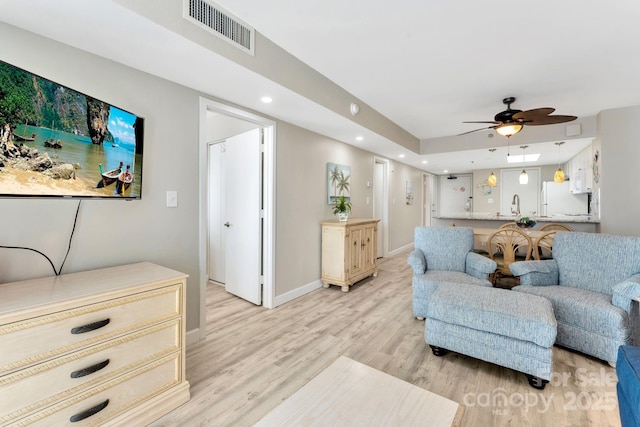 living room featuring ceiling fan, sink, and light wood-type flooring