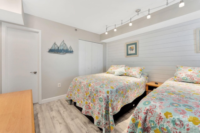 bedroom featuring a closet, rail lighting, wood walls, and light hardwood / wood-style flooring