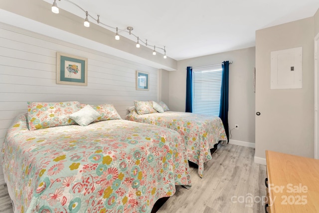 bedroom featuring track lighting, wooden walls, electric panel, and light hardwood / wood-style floors