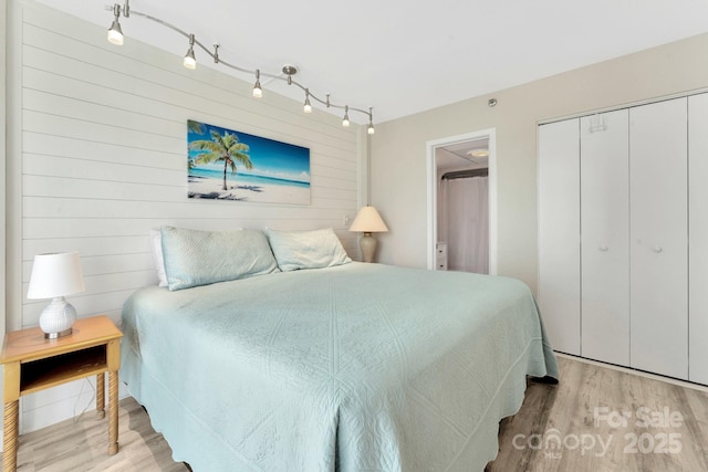 bedroom with track lighting, light hardwood / wood-style floors, a closet, and wooden walls