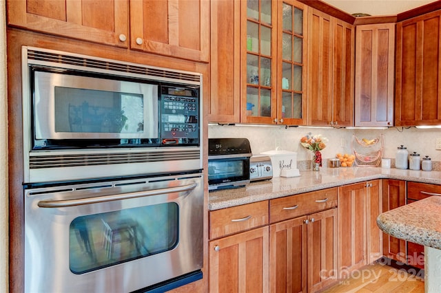 kitchen with backsplash, light stone counters, stainless steel appliances, and light hardwood / wood-style floors