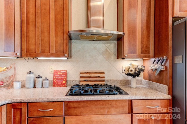 kitchen featuring light stone countertops, wall chimney range hood, tasteful backsplash, stainless steel fridge, and gas stovetop