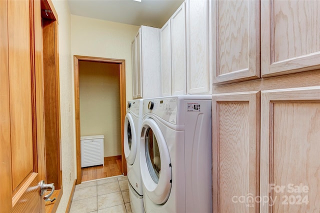 clothes washing area featuring light tile patterned floors, washing machine and dryer, and cabinets