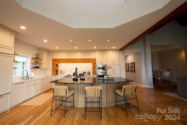 kitchen with light hardwood / wood-style floors, white cabinetry, sink, and a kitchen bar