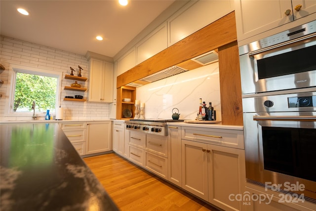 kitchen featuring stainless steel appliances, backsplash, light hardwood / wood-style floors, and white cabinetry